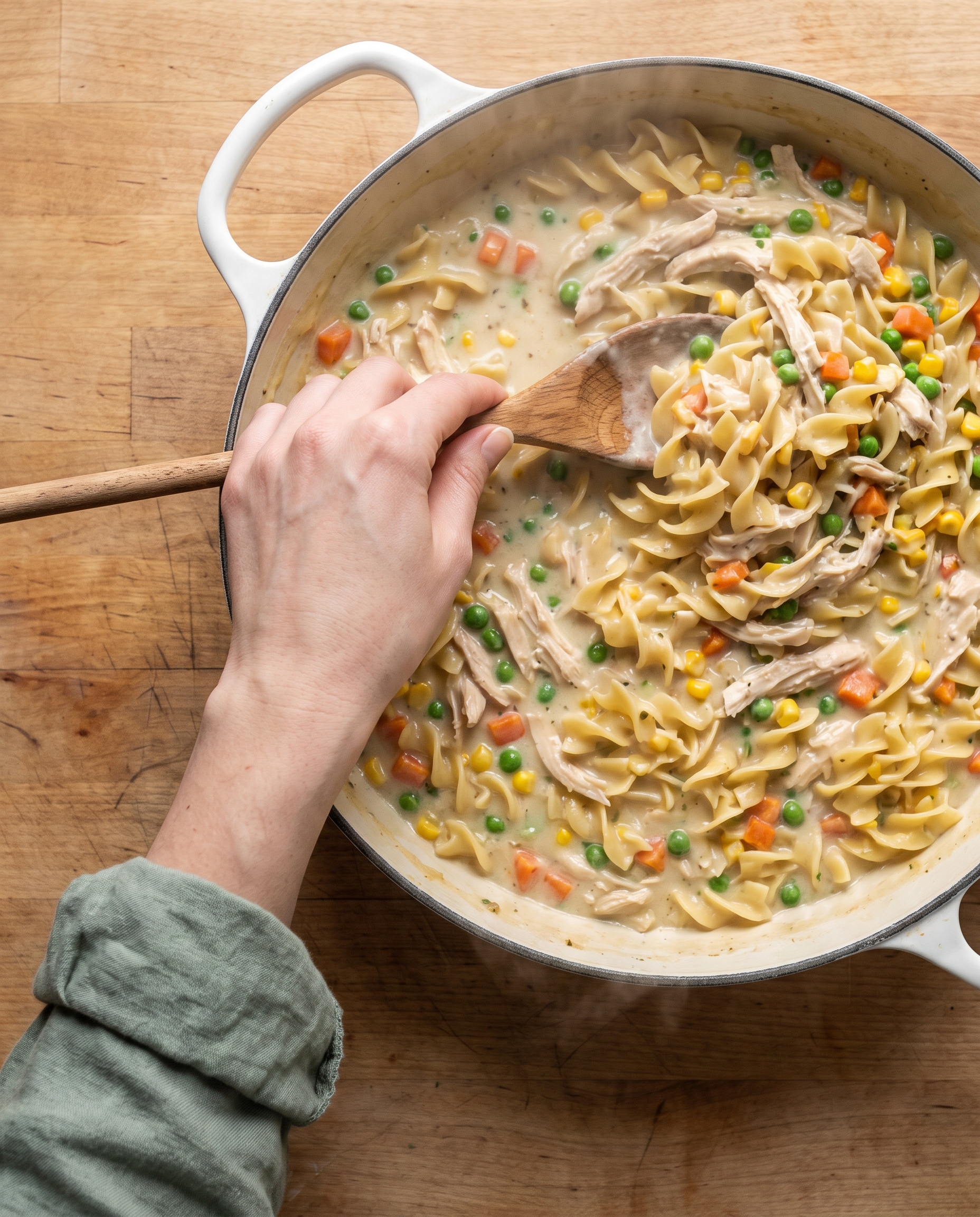 Stirring creamy chicken pot pie pasta in a white skillet