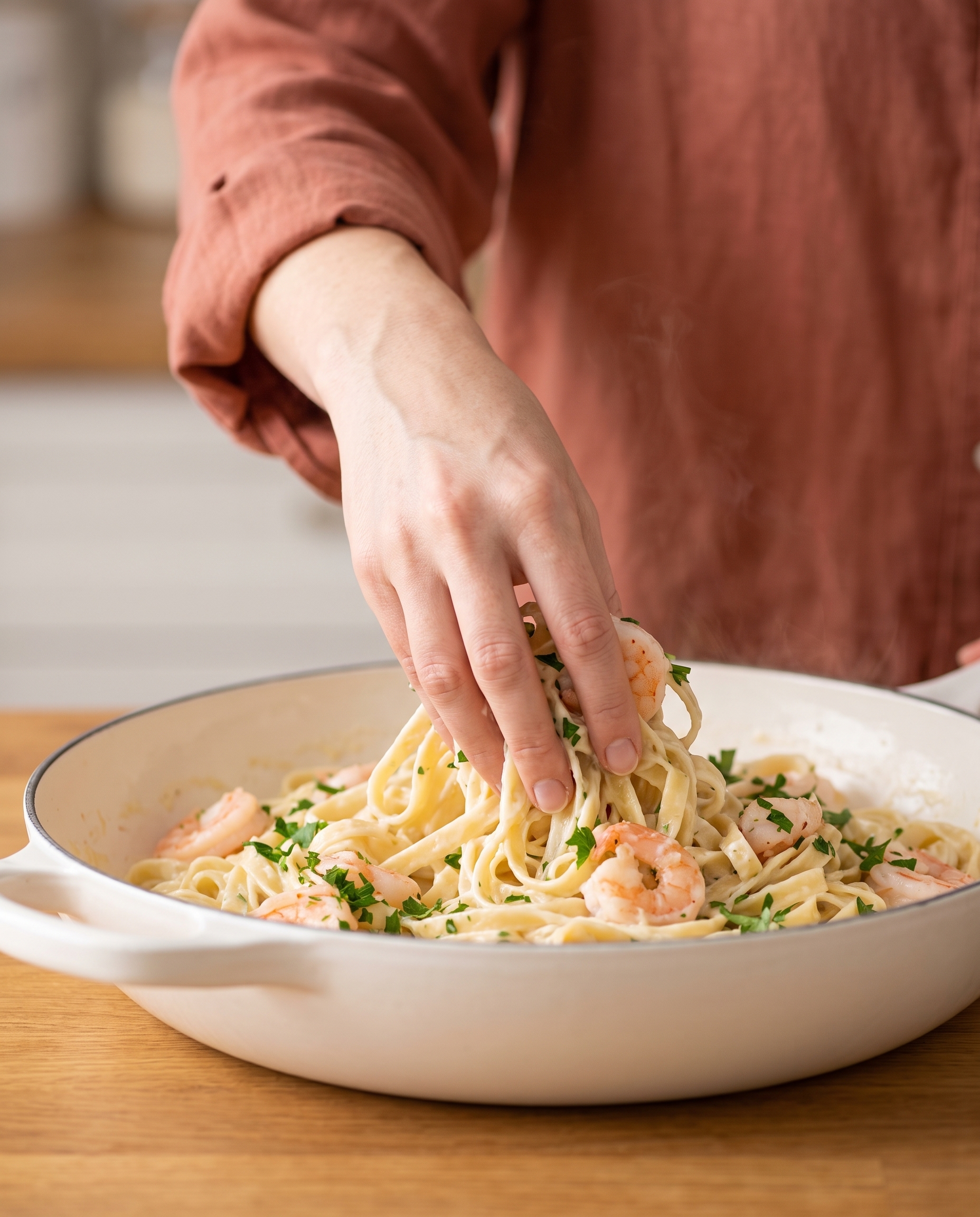 Hand tossing fettuccine in creamy alfredo sauce in a skillet