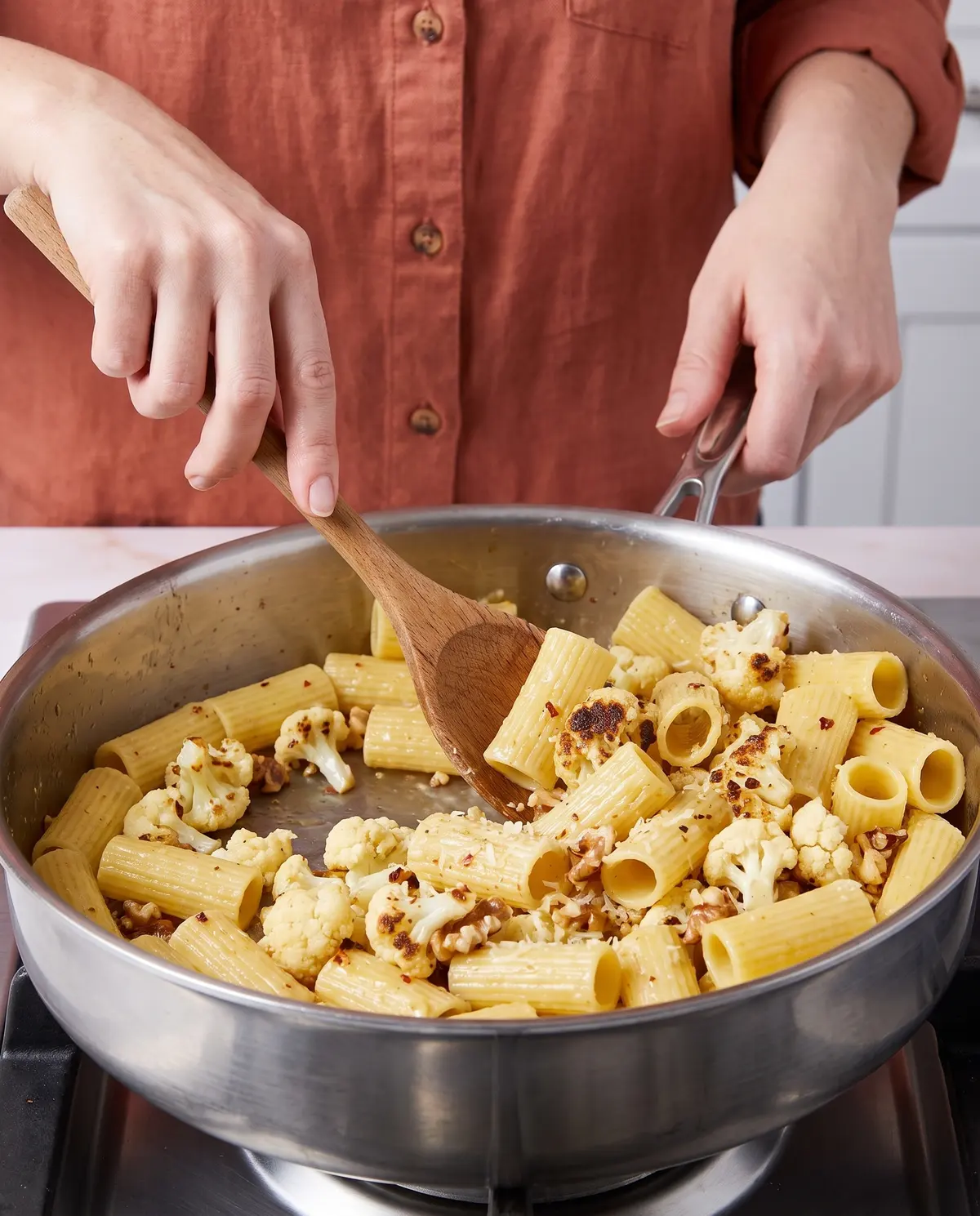 A cook tossing rigatoni and roasted cauliflower in a pan