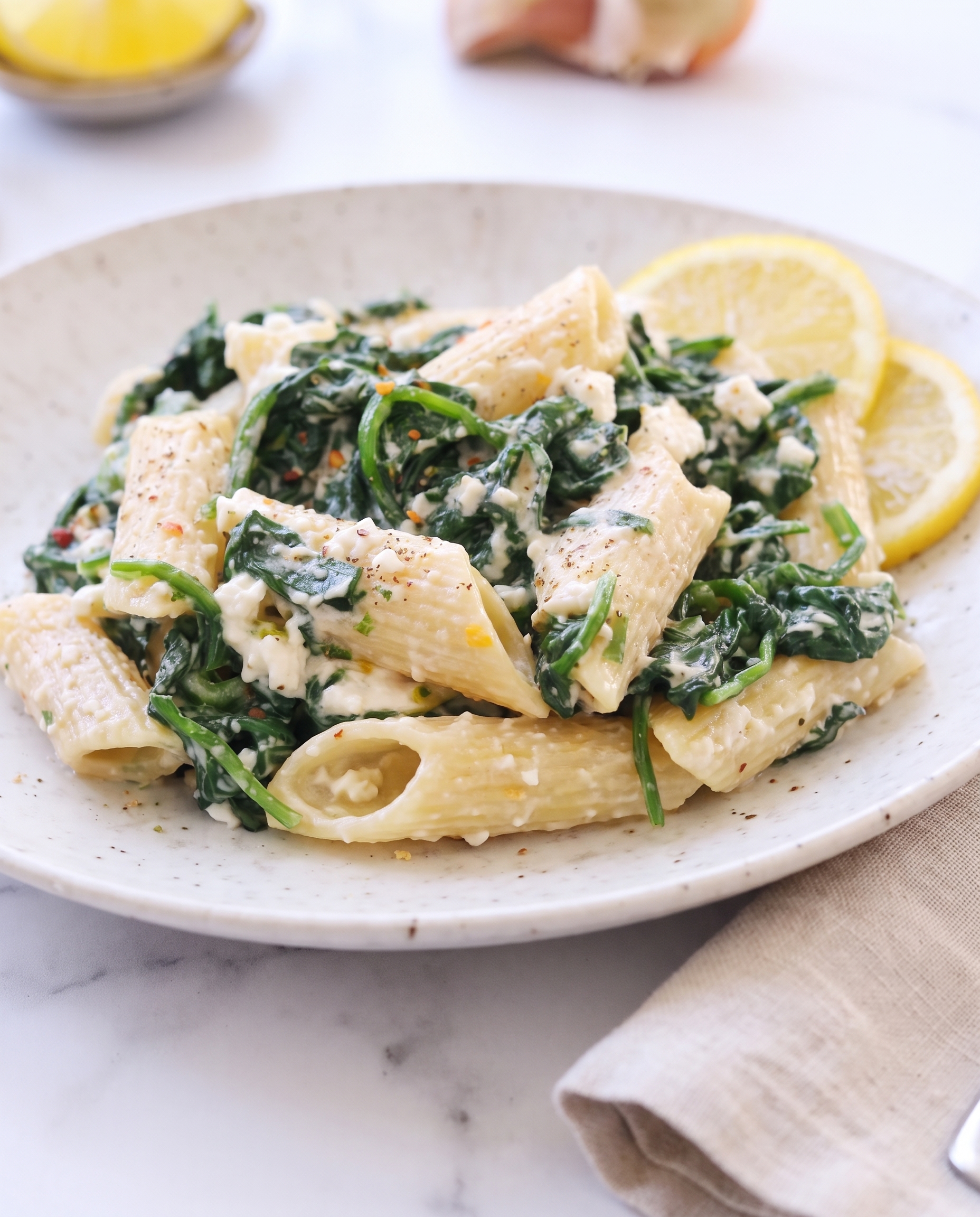 Creamy spinach and feta pasta close-up with lemon slice on a plate