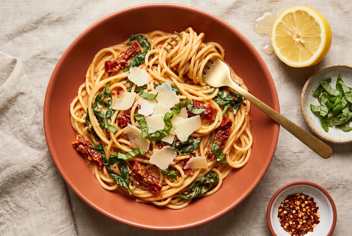 Creamy sun-dried tomato spaghetti in a terracotta bowl with torn basil leaves and shaved parmesan