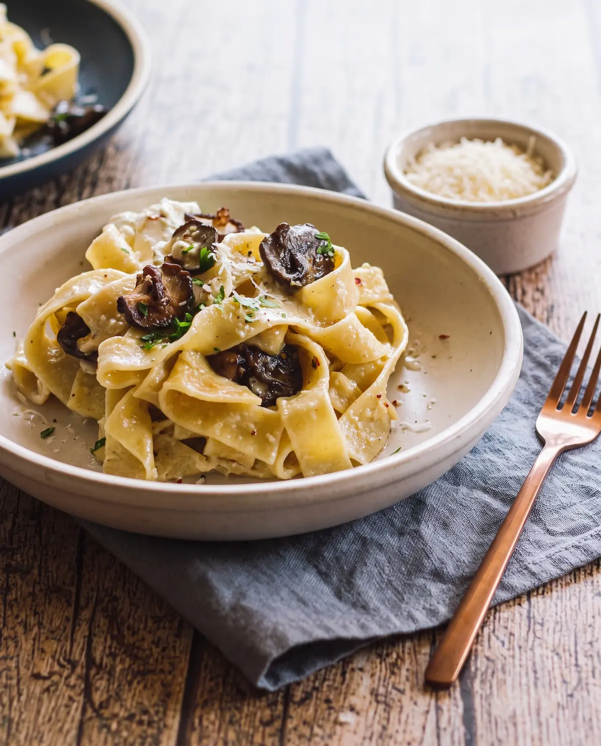 Side angle of garlic butter mushroom pappardelle in a stoneware bowl with copper fork