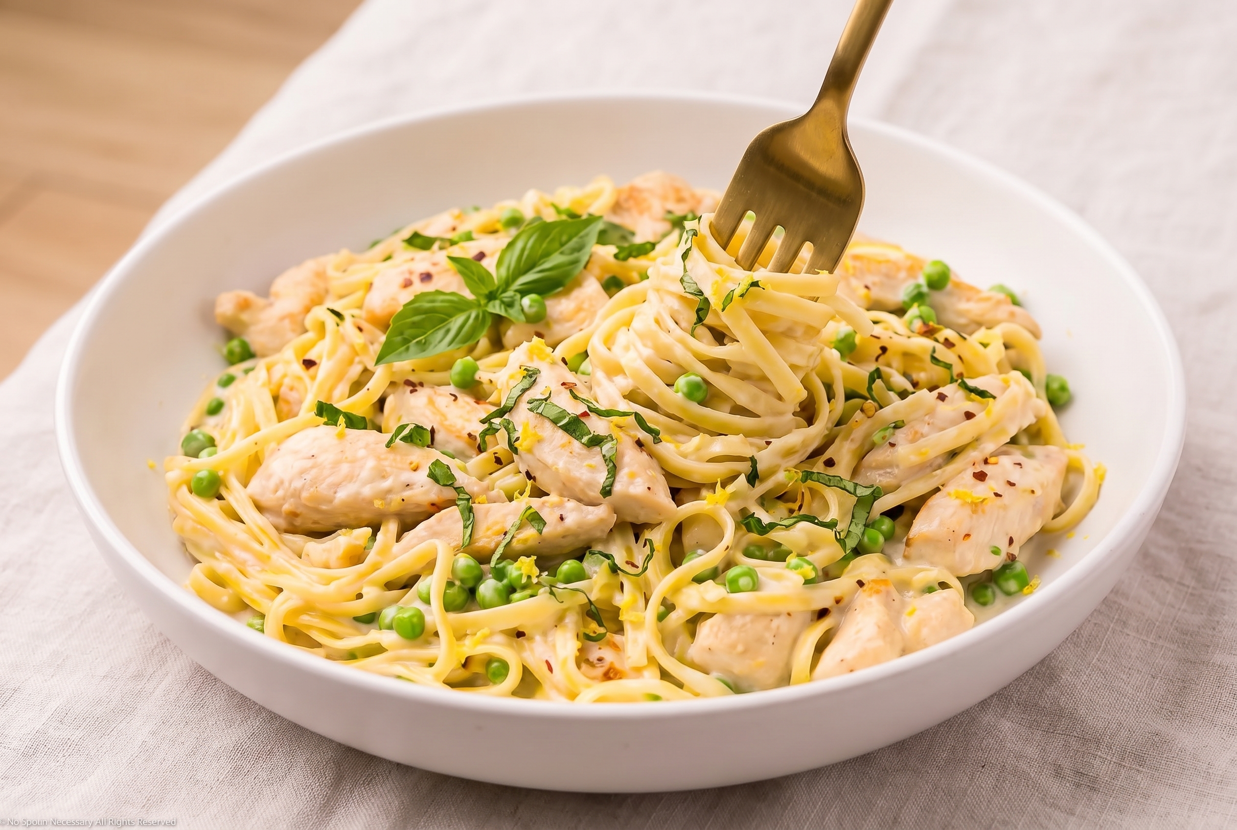 Creamy lemon basil pea pasta twirled on a fork in a white ceramic bowl
