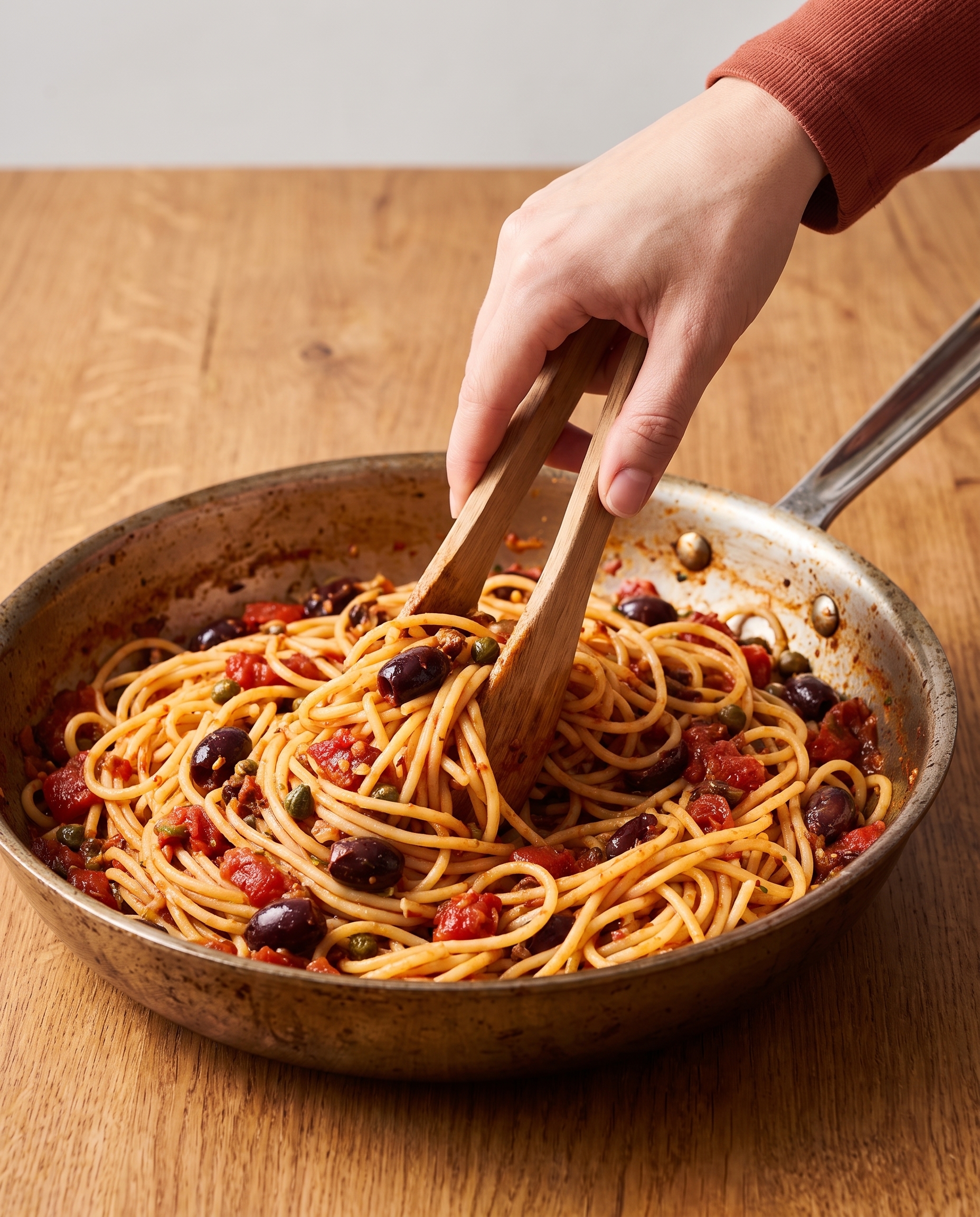 Tossing spaghetti with puttanesca sauce in a skillet