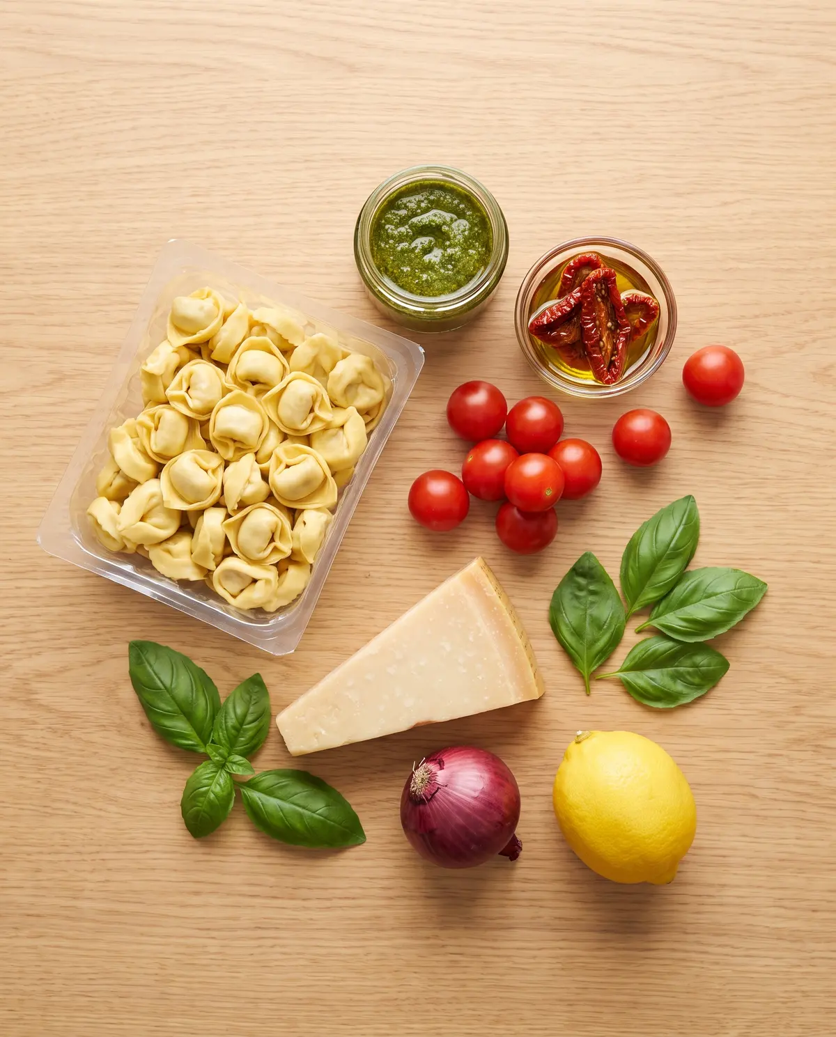 Ingredients for sun-dried tomato pesto tortellini salad arranged on a wood table