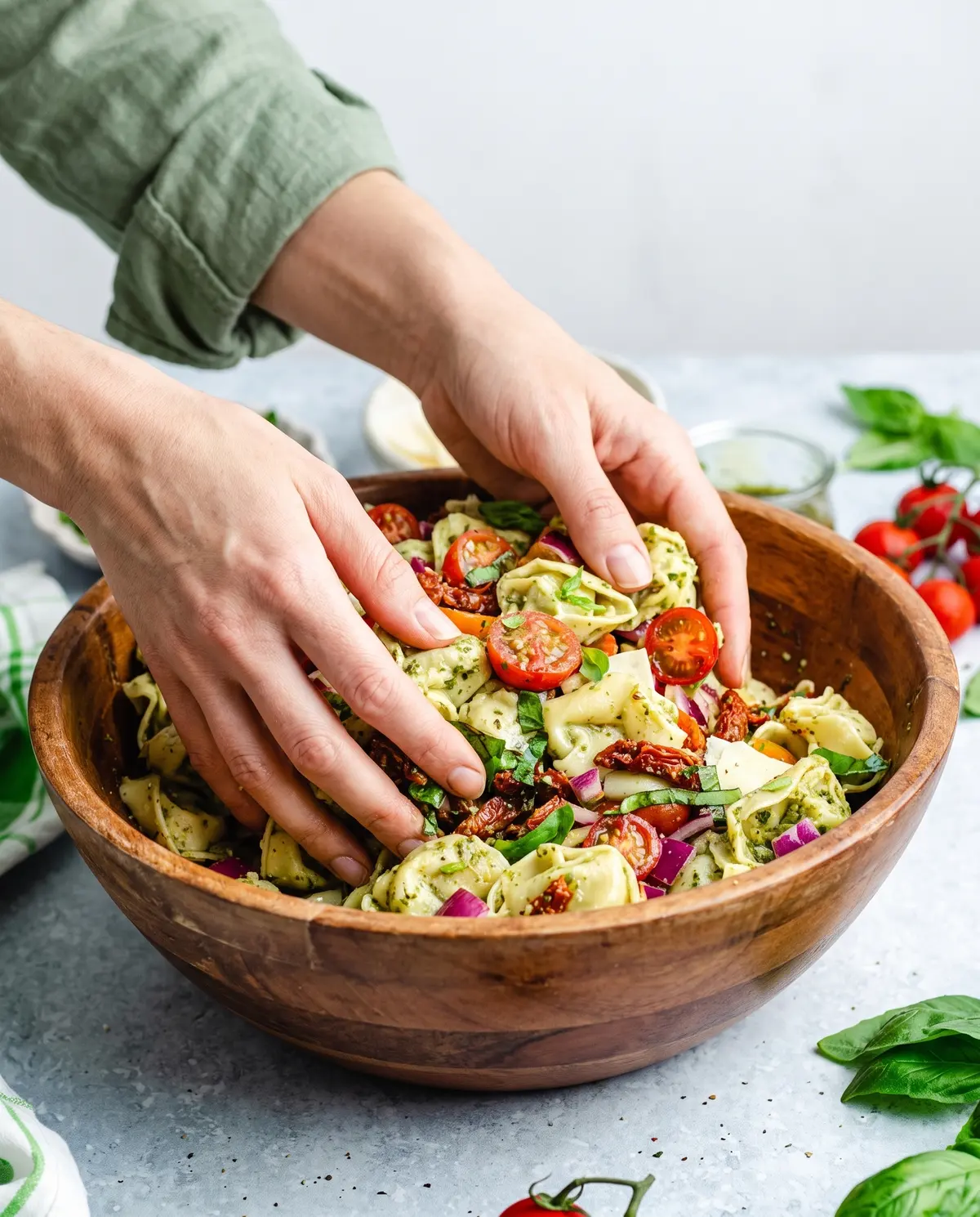 A cook tossing tortellini salad with sun-dried tomatoes in a wooden bowl