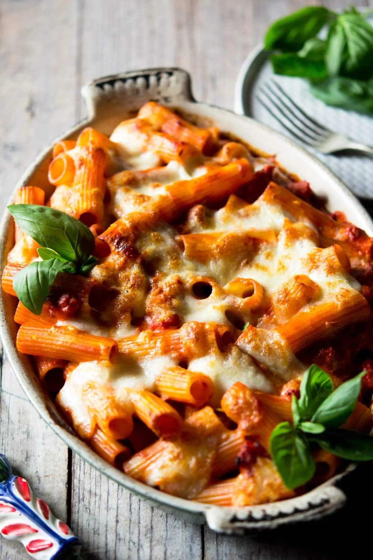 A baked pasta dish with spicy Italian sausage, tomato sauce, and melted mozzarella on top in a ceramic baking dish