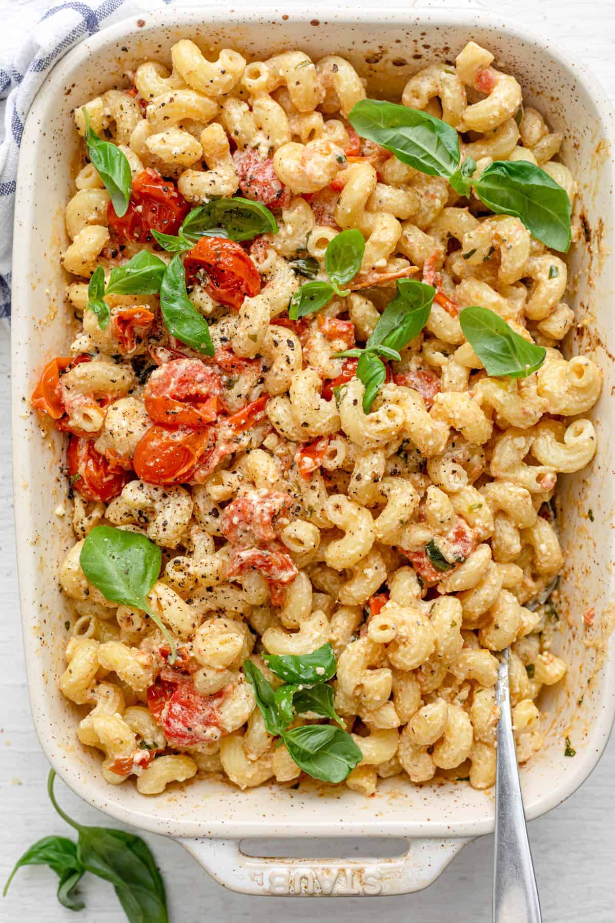 A bubbling baked feta pasta in a ceramic baking dish — roasted cherry tomatoes, a golden-brown block of feta, and fresh basil over bowtie pasta