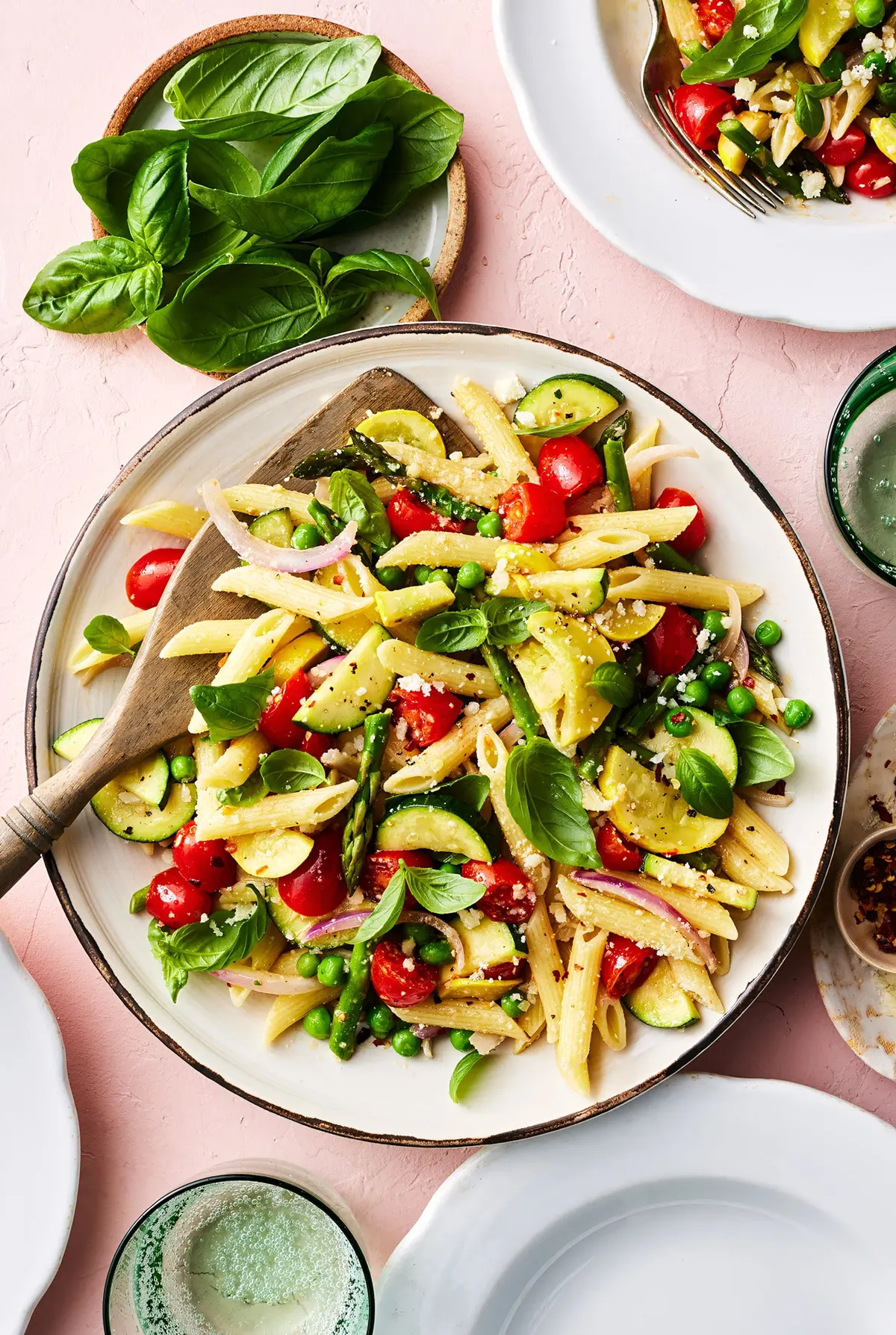 A colorful bowl of pasta primavera with yellow squash, zucchini, asparagus, cherry tomatoes, and fresh basil