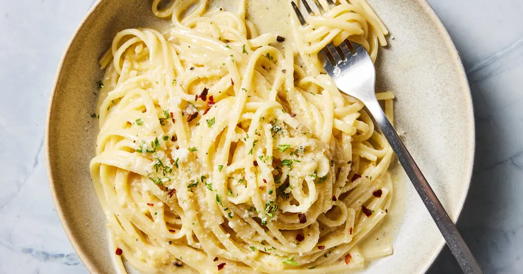 A bowl of creamy garlic parmesan pasta — tube pasta in a silky white parmesan sauce, topped with fresh parsley