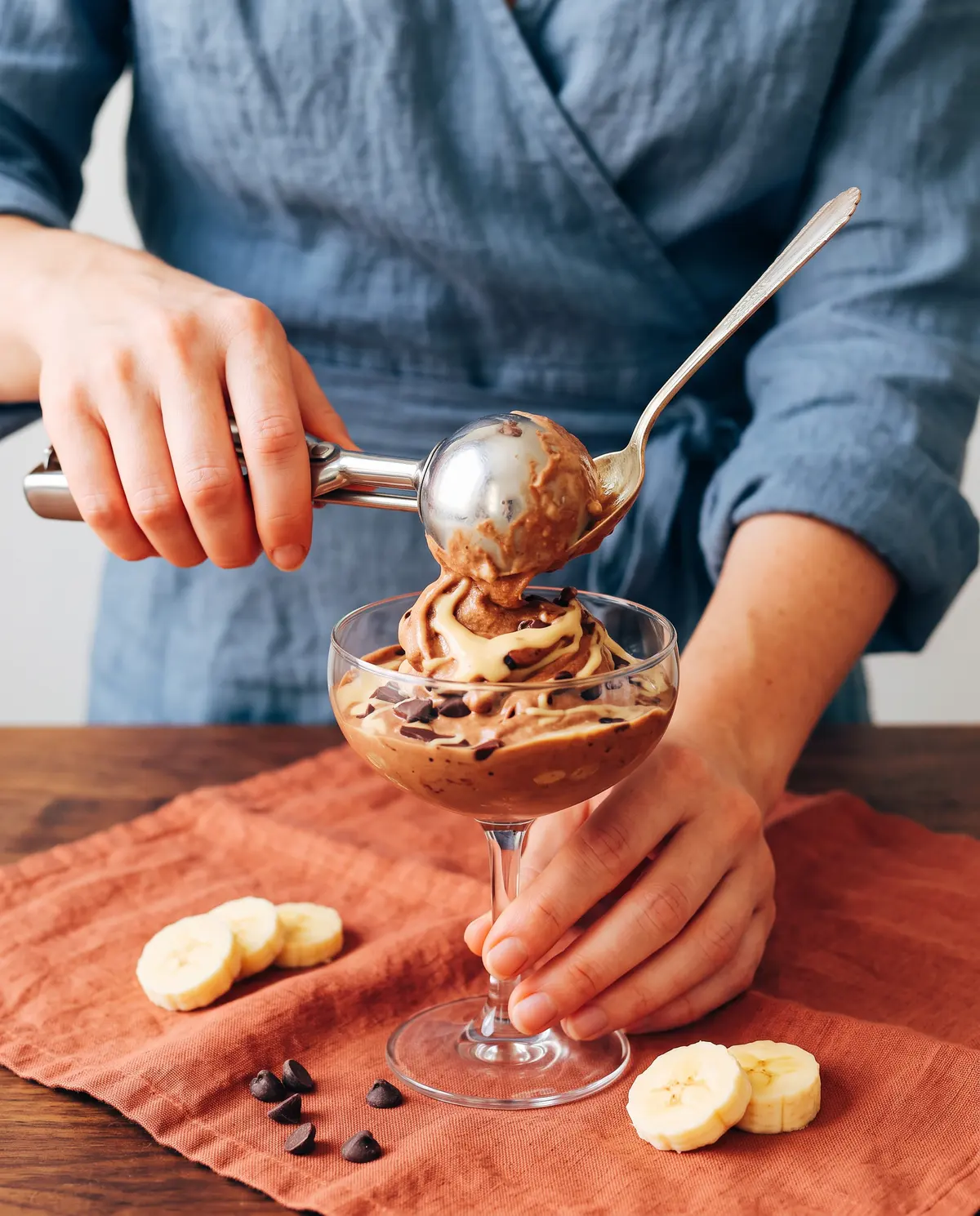 Feminine hands portioning chocolate banana nice cream into a coupe glass