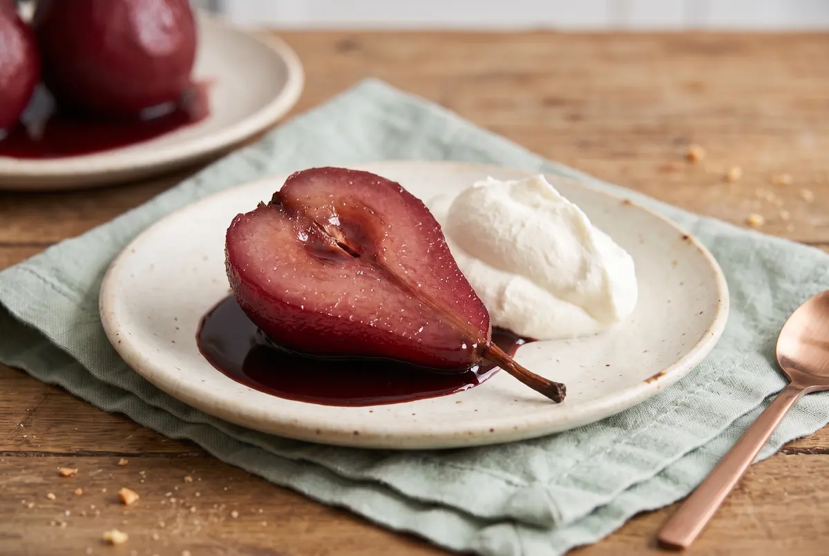 A poached pear sliced in half showing the inside, served with chocolate sauce