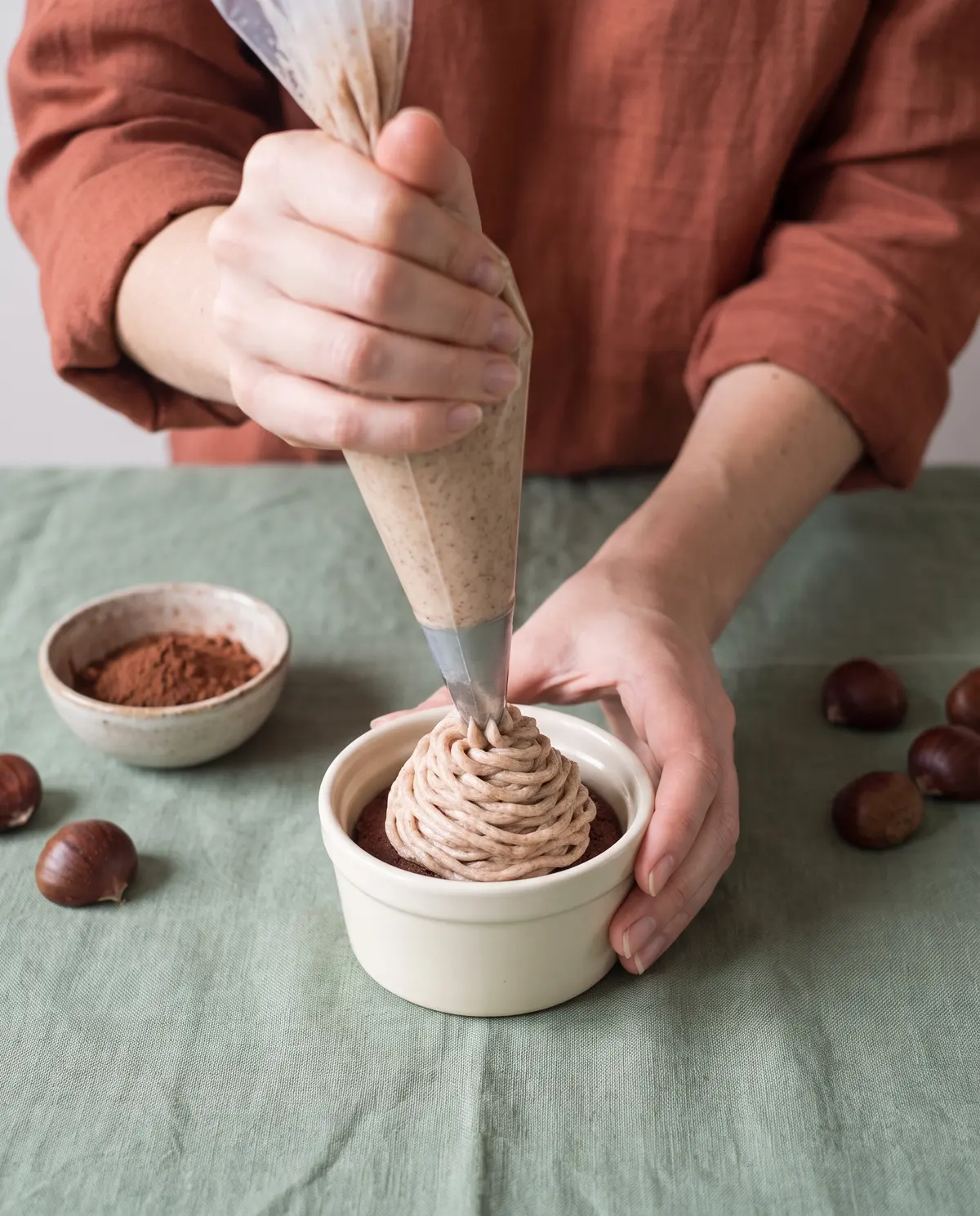Piping chestnut cream onto the chocolate meringue base in a small ceramic ramekin