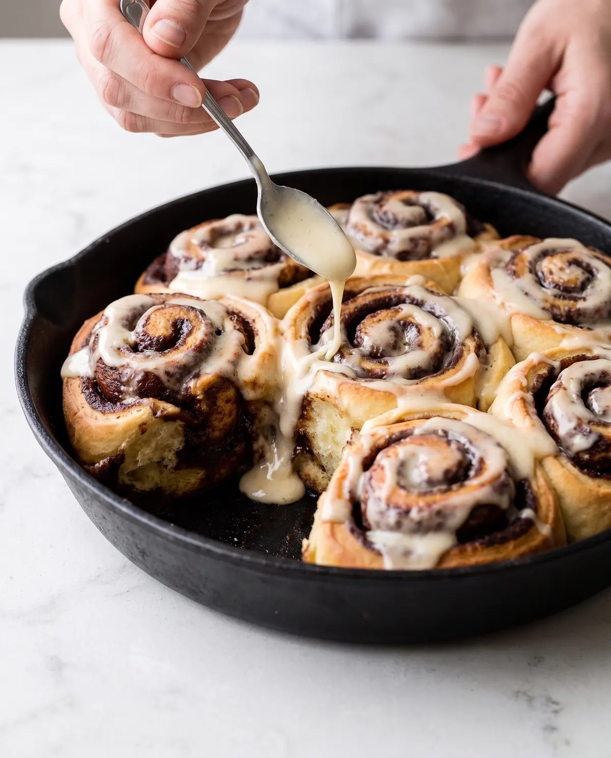 Hands drizzling espresso glaze over chocolate cinnamon rolls