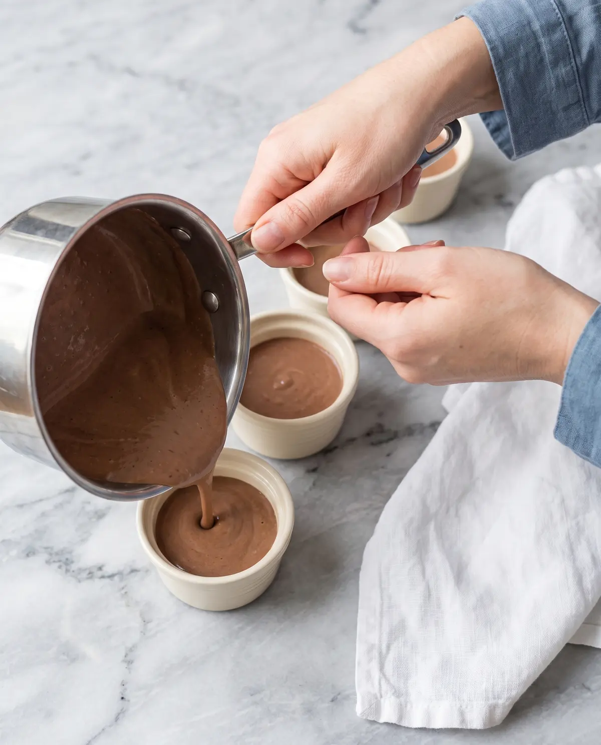 Hands pouring warm chocolate coconut cream into ramekins