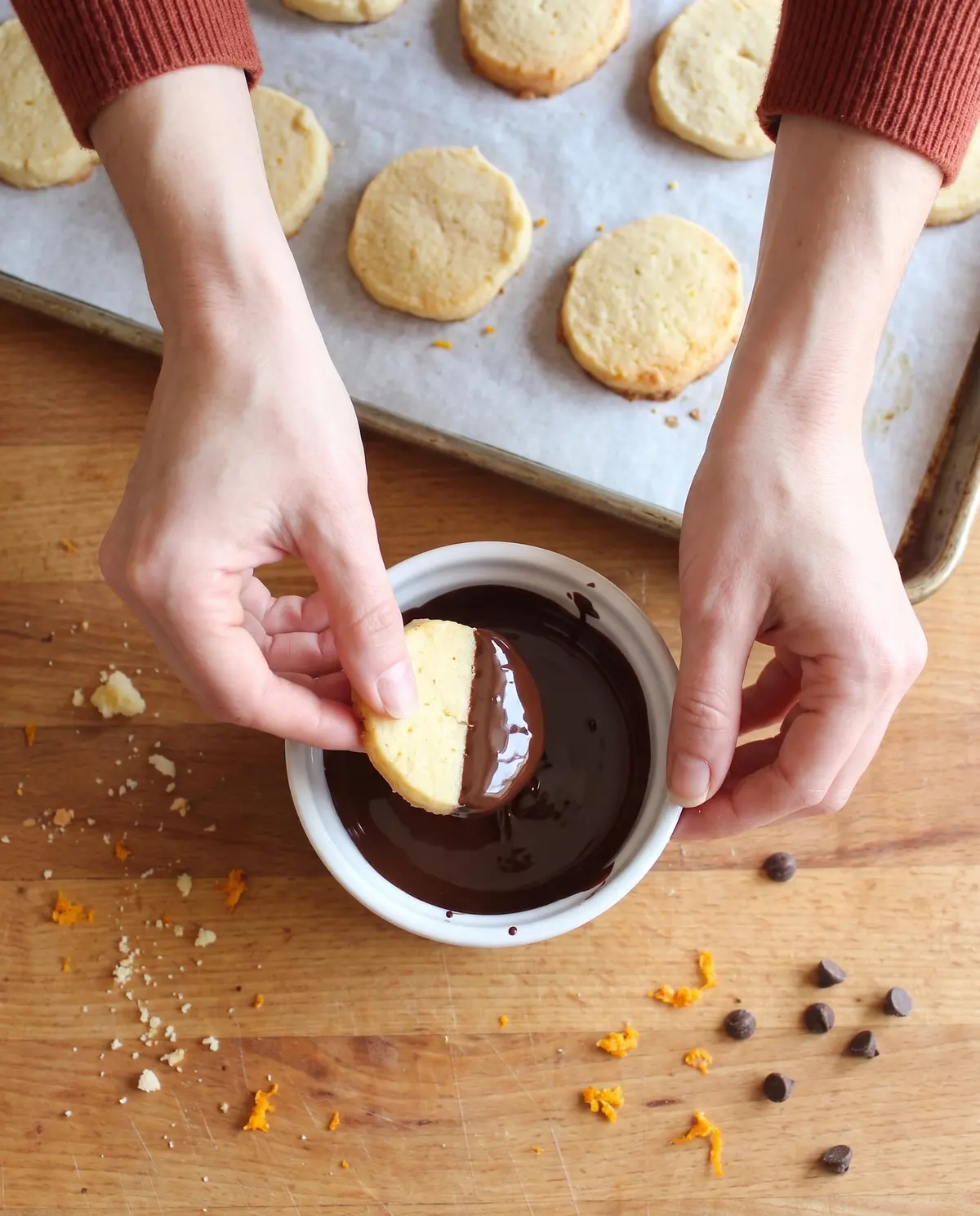 Hands dipping an orange shortbread cookie into a small bowl of melted dark chocolate
