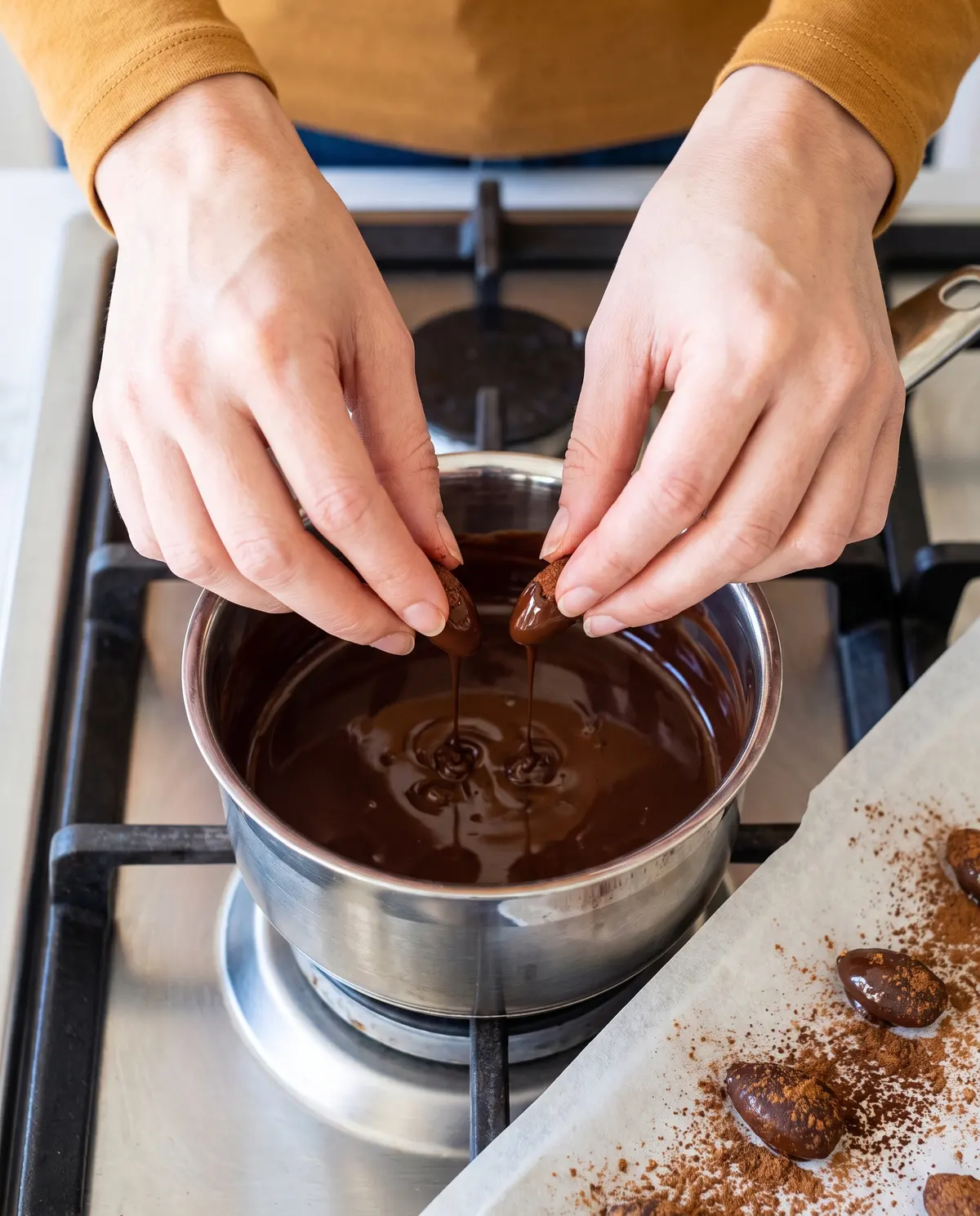 Hands dipping almonds into melted chocolate on the stovetop