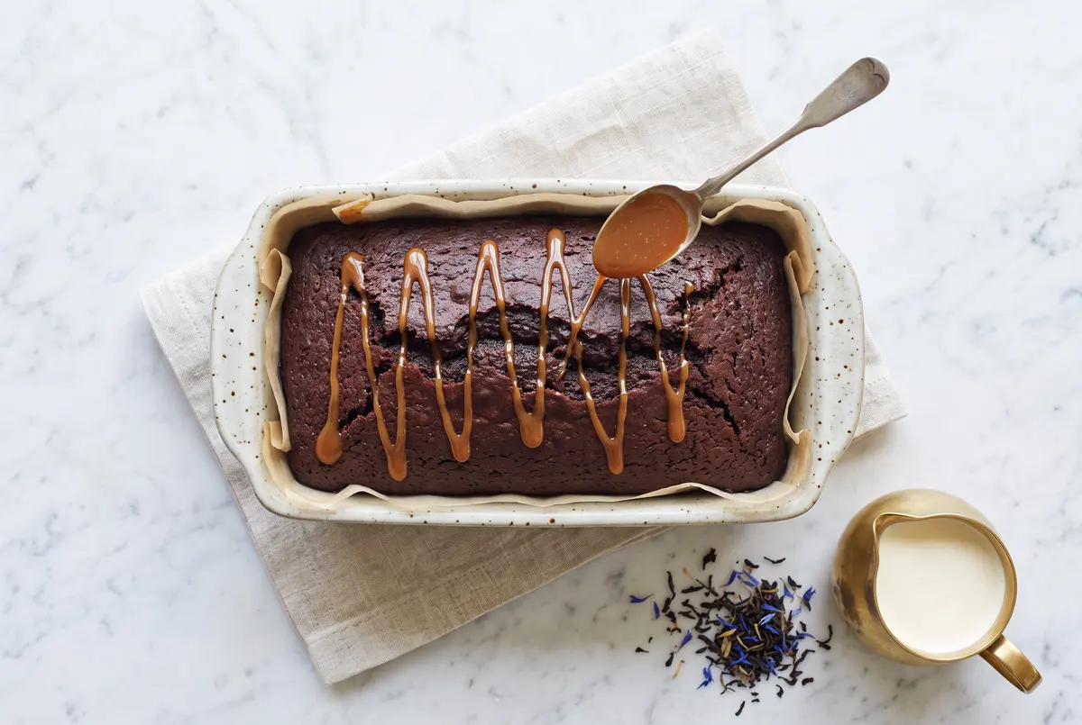 Whole uncut chocolate Earl Grey loaf cake with caramel being drizzled on top in a zigzag pattern