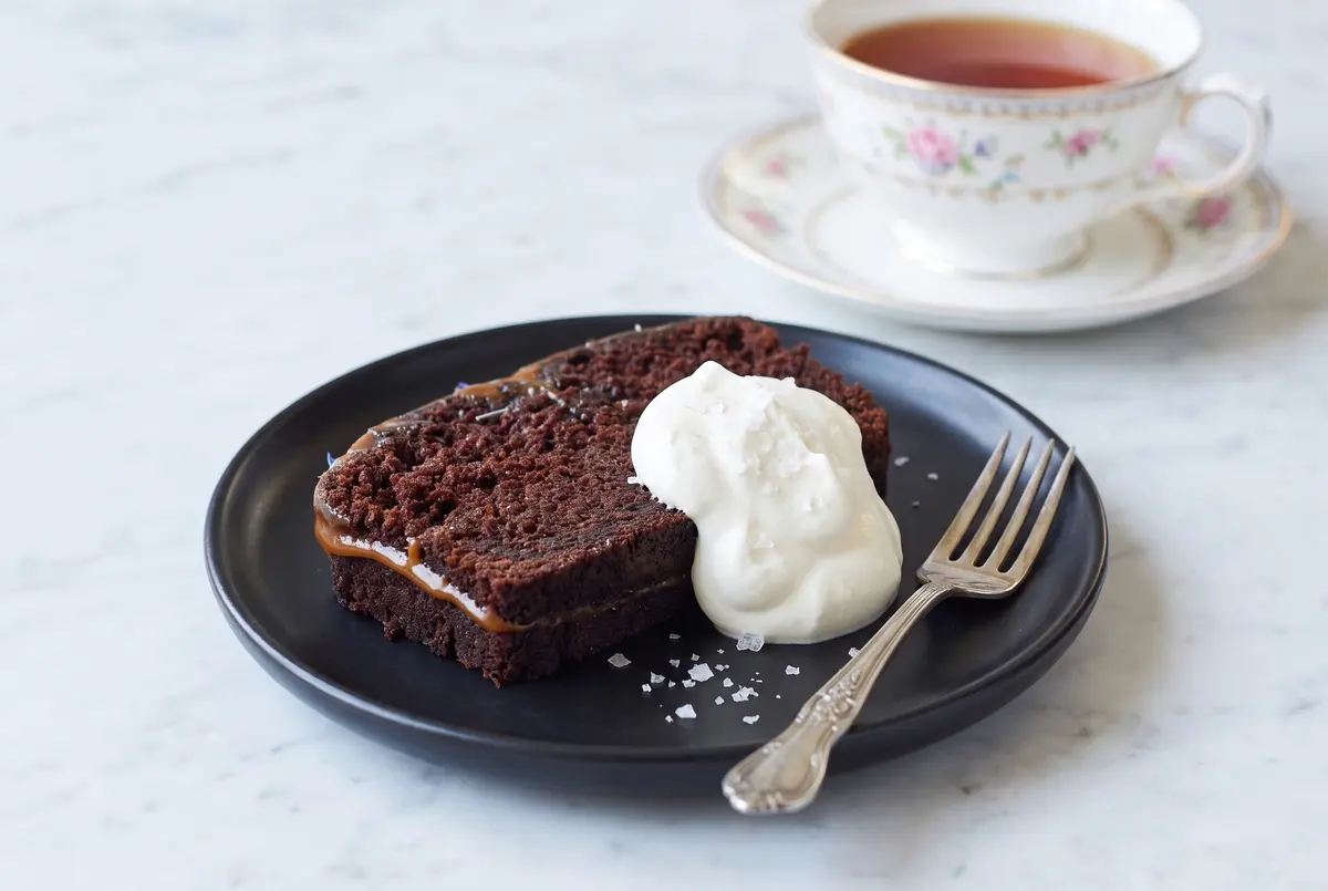 A single slice of chocolate Earl Grey loaf cake on a black plate with whipped cream