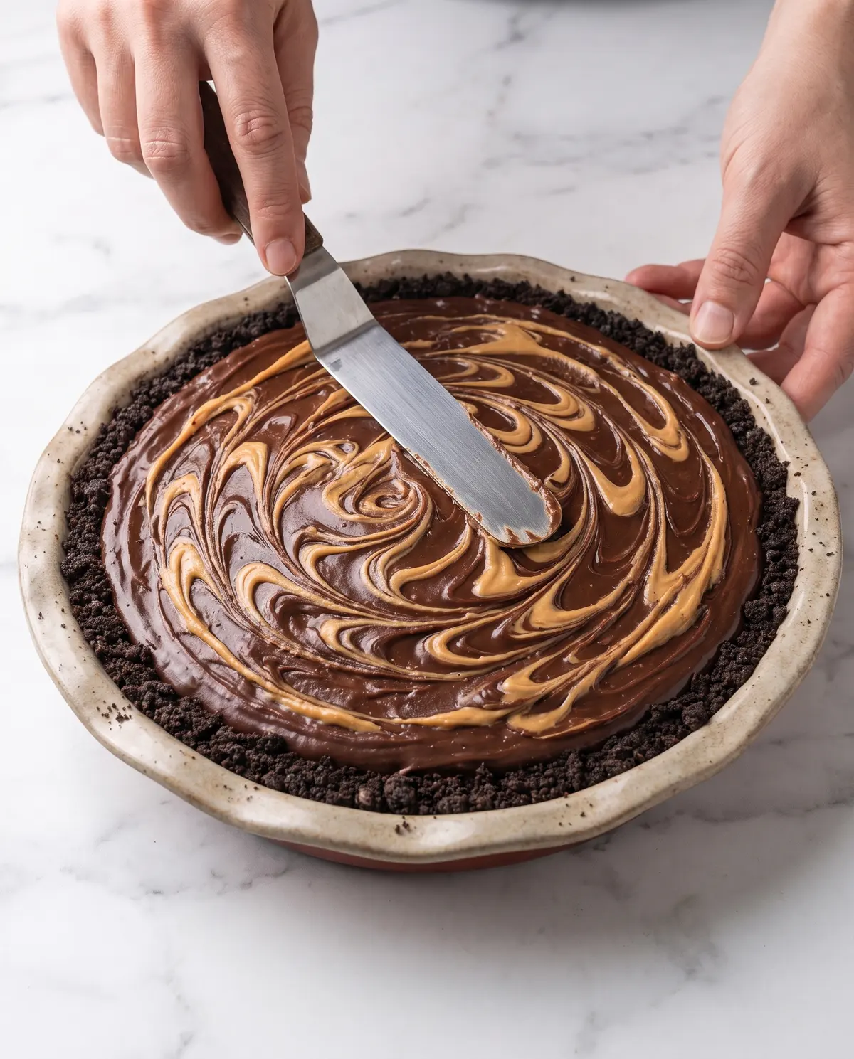 Hands spreading peanut butter filling into Oreo crust