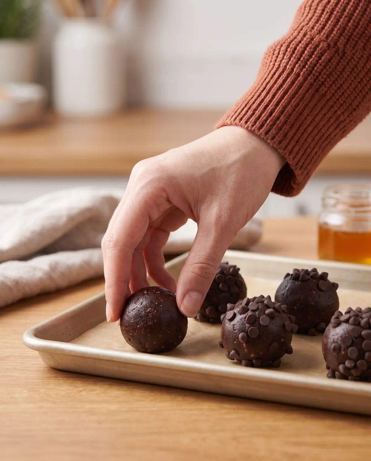 A hand rolling a chocolate protein ball on a parchment-lined baking sheet