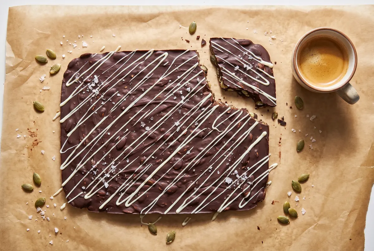 Chocolate pumpkin seed bark in a single slab on parchment with espresso