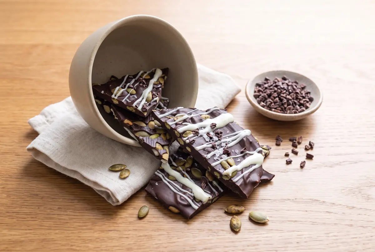 Broken dark chocolate pumpkin seed bark spilling from a stoneware bowl