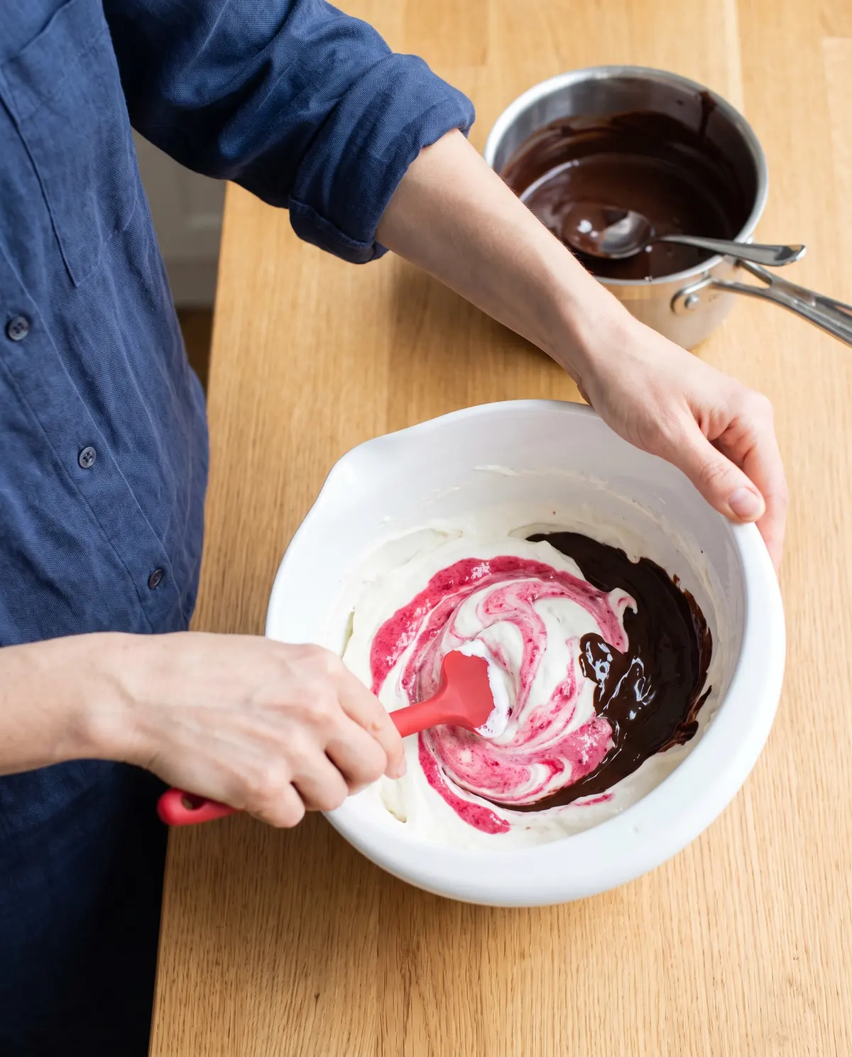 Hands folding raspberry puree into the semifreddo base in a white bowl