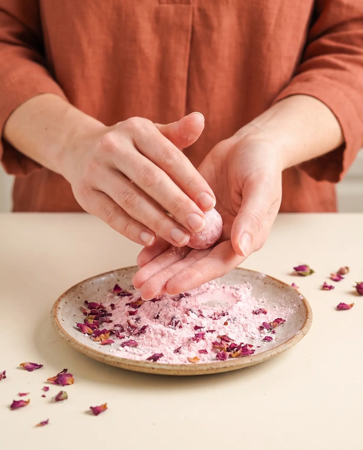 Hands rolling a pink truffle in powdered sugar on a small plate